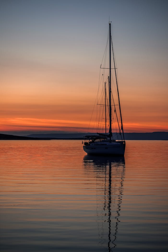 gallery-3 A sailboat silhouetted against a vibrant sunset on Sardinia's serene waters.