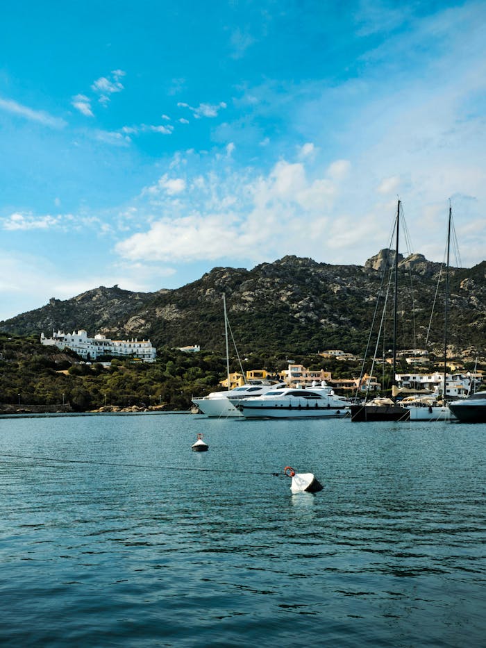 Opulent-Mediterra-Sardinia-Yacht-Charter-Maddalena Luxury yachts docked in a scenic Mediterranean harbor with rugged coastal hills, representing private marine expeditions in the Maddalena archipelago.