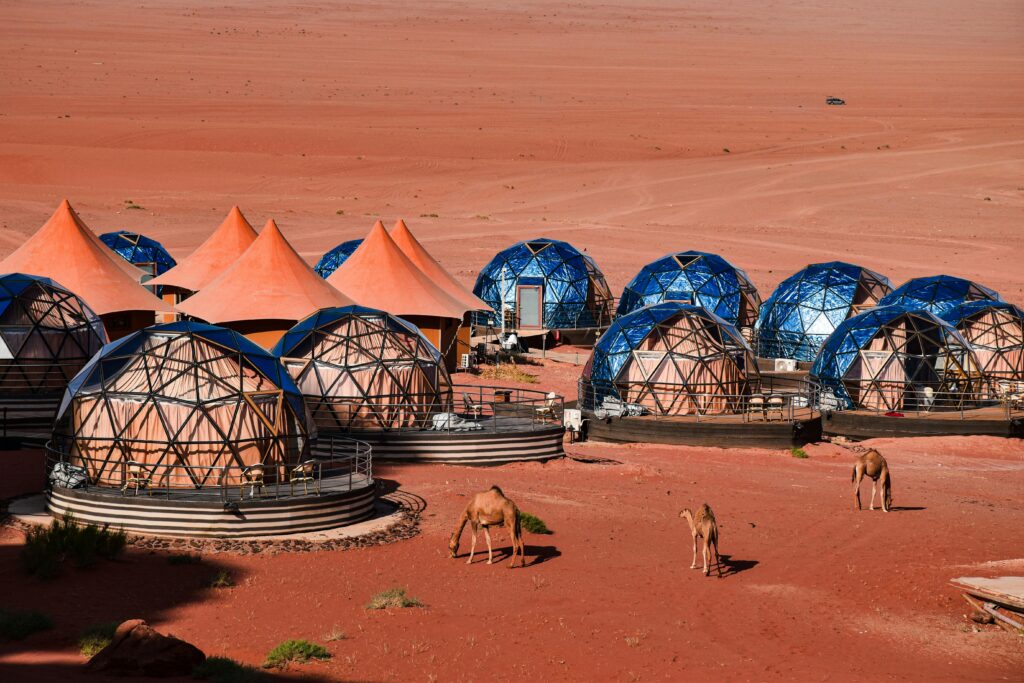 Luxury desert glamping site with blue dome tents in the red sand dunes of the Sahara at sunset.