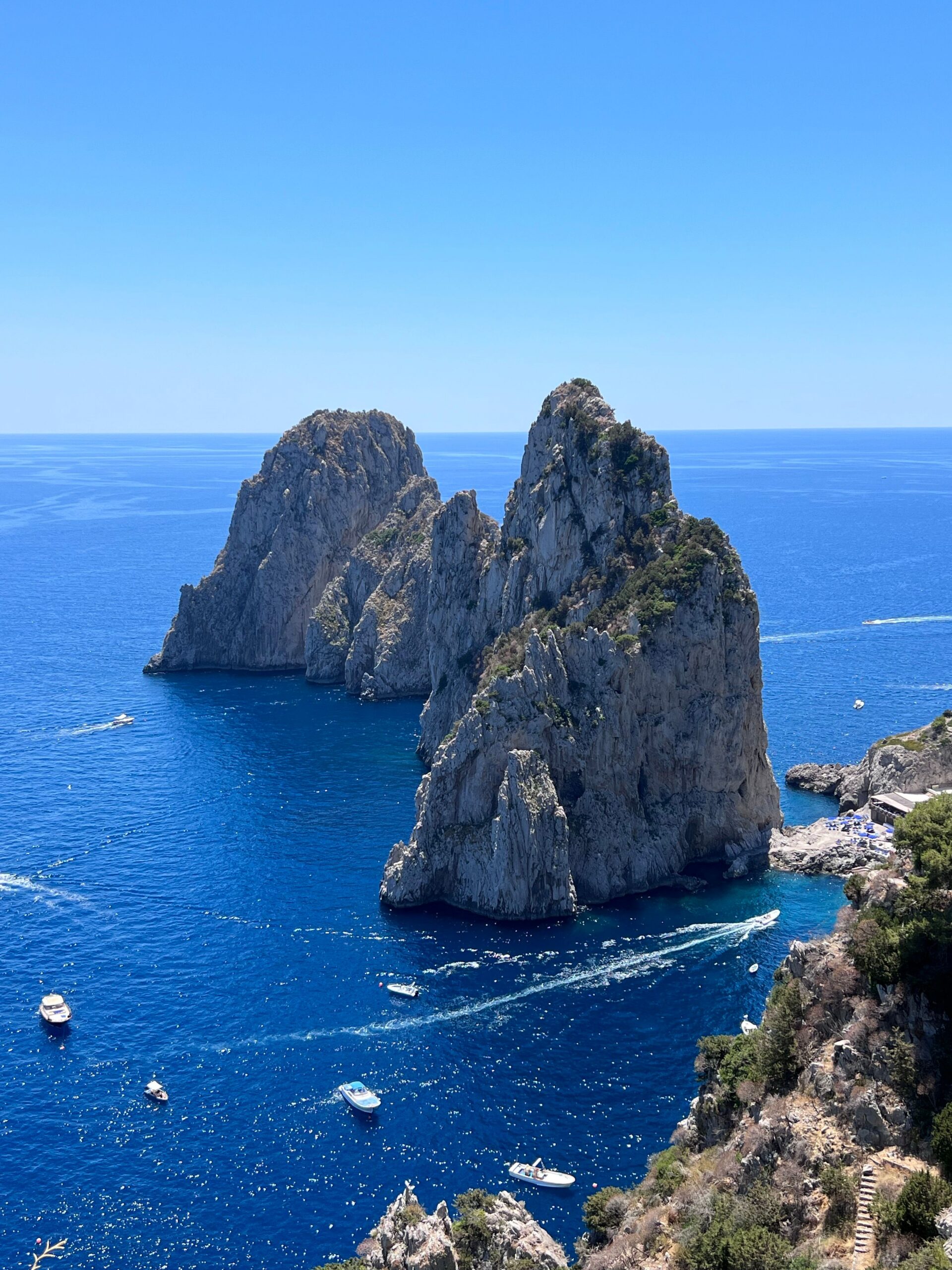 Faraglioni sea stacks off Capri, Italy, seen from a cliffside viewpoint with boats crossing the turquoise water